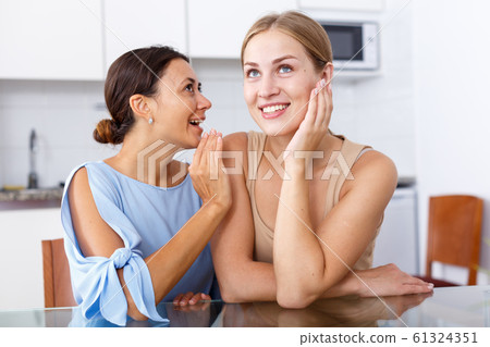 Portrait of young smiling girlfriends sharing secrets and chatting at table 61324351
