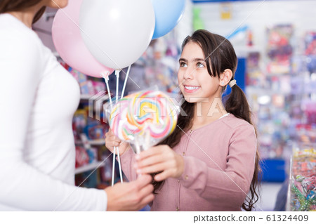 Portrait of smiling girl with balloons receives lollipop Portrait of smiling girl with balloons receives lollipop 61324409