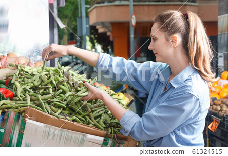 Female is choosing peas on the shelves in the market. 61324515