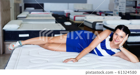 Customer girl is posing lying on new mattress before buying it in shop. Customer girl is posing lying on new mattress before buying it in shop. 61324580