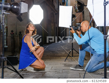 Professional photo shooting outdoors. Attractive female model posing to photographer on city street Professional photo shooting outdoors. Attractive female model posing to photographer on city street 61324589