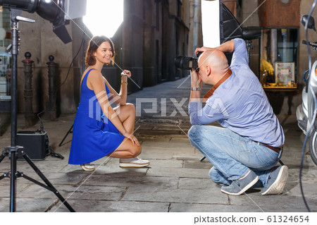 Professional photo shooting outdoors. Attractive female model posing to photographer on city street Professional photo shooting outdoors. Attractive female model posing to photographer on city street 61324654