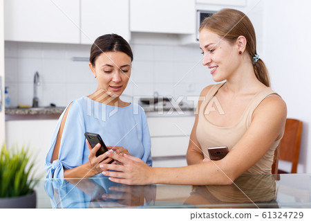 Portrait of young smiling girlfriends using smartphones and chatting at table 61324729