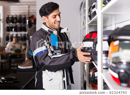 Man in moto jacket is choosing new helmet for motorbike in the store. Man in moto jacket is choosing new helmet for motorbike in the store. 61324743