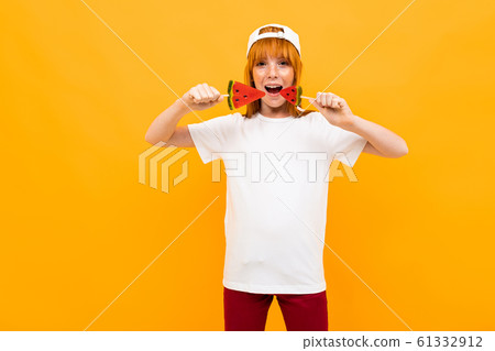 Happy girl with red hair in white t-shirt with white cap smiles with watermelon lolipops isolated on 61332912