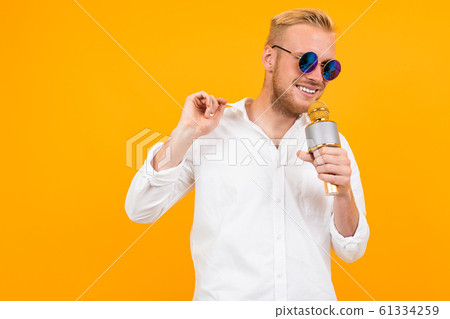 Beautiful caucasian man with glasses sings songs in karaoke with microphone isolated on yellow Beautiful caucasian man with glasses sings songs in karaoke with microphone isolated on yellow 61334259