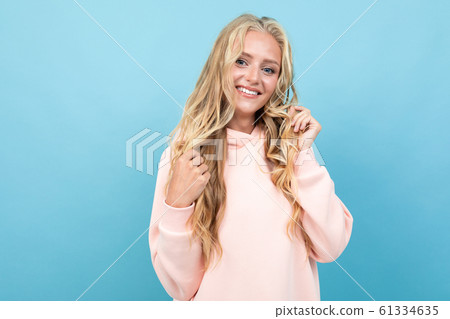 Caucasian woman with blonde hair in pink hoody smiles isolated on blue background 61334635