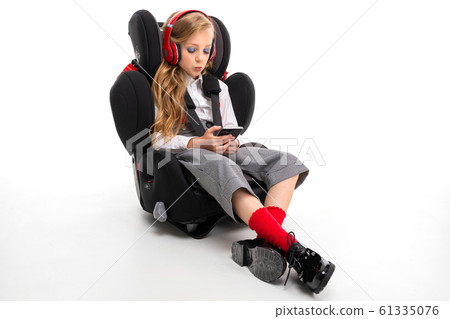 A little girl with makeup and long blonde hair sits on a car baby chair 61335076