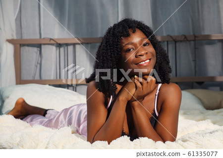 smiling African American girl in nightgown lying on large white bed in early morning 61335077