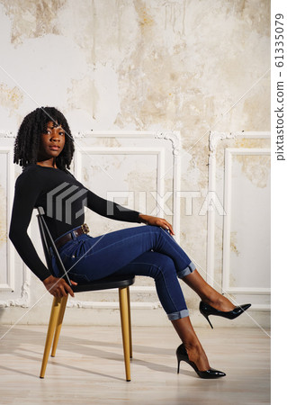 exciting black lady in blue jeans sits on brown wooden chair 61335079