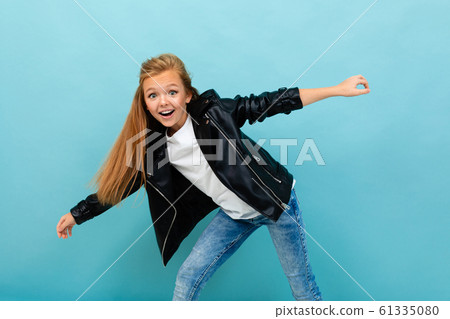 Beautiful caucasian teenager girl in black jacket and jeans dances isolated on blue background 61335080