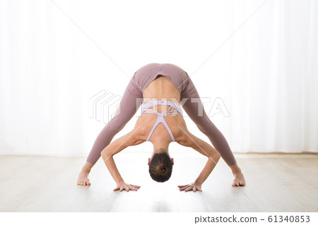 Portrait of gorgeous active sporty young woman practicing yoga in studio. Beautiful girl practice Dandayamana Bibhaktapada Paschimotthanasana, standing separate leg stretching pose 61340853