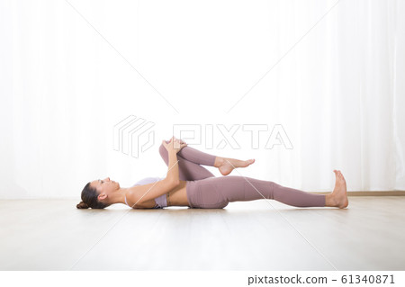 Portrait of gorgeous active sporty young woman practicing yoga in studio. Beautiful girl practice Pavana Muktasana, wind removing yoga pose. Healthy active lifestyle, working out indoors in gym 61340871