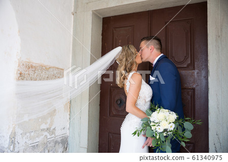 The Kiss. Bride and groom kisses tenderly in front of church portal. 61340975