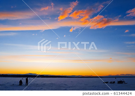silhouettes of fishermen on winter fishing on the ice of the river 61344424