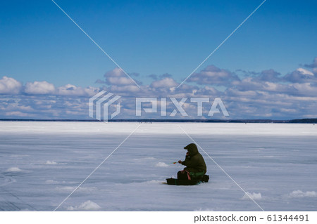 fisherman with a fishing rod sitting and fishing in winter fisherman with a fishing rod sitting and fishing in winter 61344491
