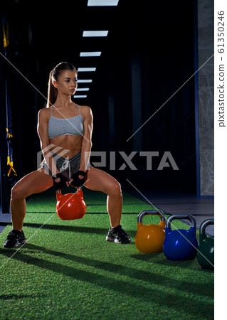 Fitnesswoman squatting with kettlebell in gym. 61350246