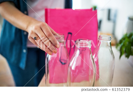 Young woman putting glass bottles in bag indoors at home, recycling concept. 61352379
