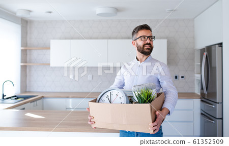 Mature man standing in unfurnished house, holding a moving box. Mature man standing in unfurnished house, holding a moving box. 61352509