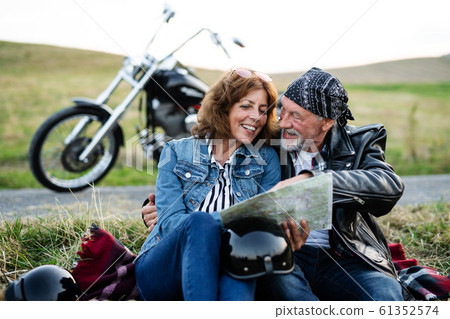 Cheerful senior couple travellers with map and motorbike in countryside. Cheerful senior couple travellers with map and motorbike in countryside. 61352574