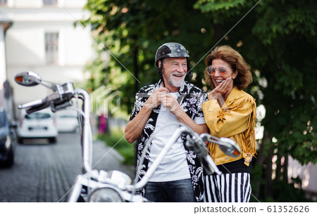 A cheerful senior couple travellers with motorbike in town. 61352626