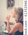 Toned picture of side view of beautiful blonde lady sitting in cafe or restaurant near window and drinking coffee 61352946
