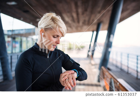 A portrait of young sportswoman with smartwatch outdoors, self-tracking. A portrait of young sportswoman with smartwatch outdoors, self-tracking. 61353037