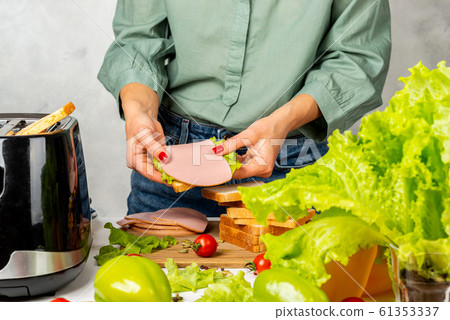 The girl holds in her hands a finished one layer of a sandwich. 61353337