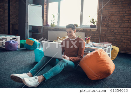 Dark-haired freelancer sitting on the floor with laptop while working Dark-haired freelancer sitting on the floor with laptop while working 61354033