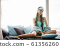 Beautiful young woman seating at window pillows in turquoise pajama set 61356260