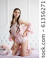 Beautiful young woman smiling sensually on the bed playing with her pink pajama set 61356271