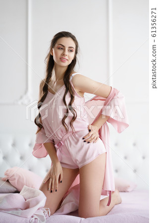 Beautiful young woman smiling sensually on the bed playing with her pink pajama set 61356271