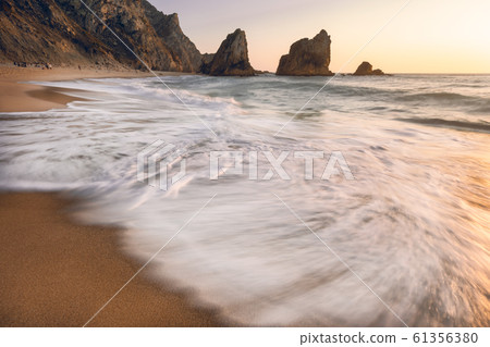 Portugal Ursa Beach. Sunset light reflection in white wave rolling towards sandy beach with silhouette of sea stacks in background Portugal Ursa Beach. Sunset light reflection in white wave rolling towards sandy beach with silhouette of sea stacks in background 61356380