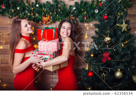 Two smiling women in red dresses with many gift boxes near christmas tree. Happy new year party. 61356534