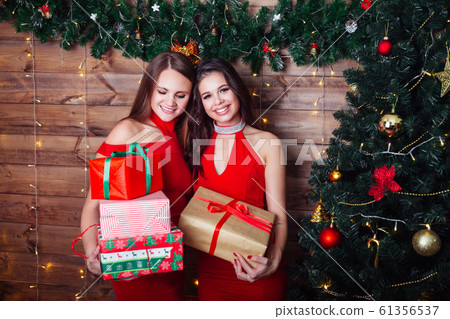 Two smiling women in red dresses with gift boxes near christmas tree. Happy new year party. Two smiling women in red dresses with gift boxes near christmas tree. Happy new year party. 61356537
