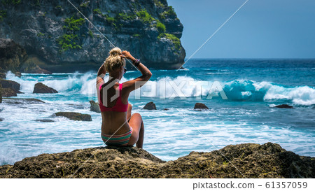 Girl sitting on the Rock and watching Huge Waves hitting Tembeling Coastline at Nusa Penida Island, Bali Indonesia 61357059