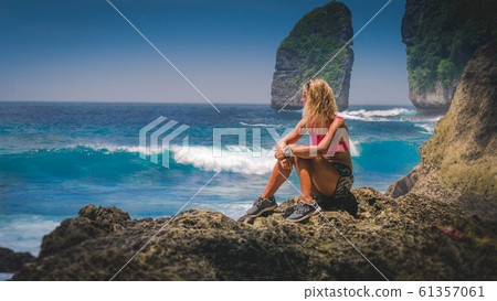 Girl sitting on the Rock and watching Huge Waves hitting Tembeling Coastline at Nusa Penida Island, Bali Indonesia Girl sitting on the Rock and watching Huge Waves hitting Tembeling Coastline at Nusa Penida Island, Bali Indonesia 61357061