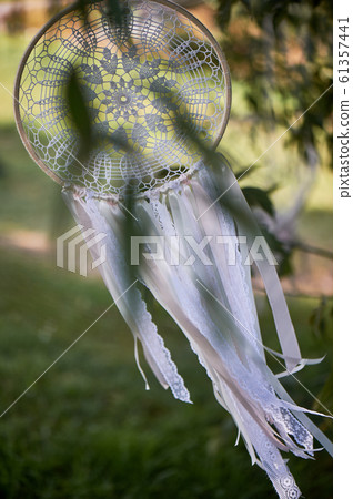 Dream catcher white color, knit. Hanging outdoors in front of the tree. 61357441