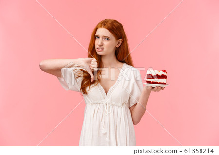 Never buy at this store again. Displeased and disappointed picky cute redhead girl frowning, grimacing from dislike, showing thumb-down in disapproval as tried awful, disgusting cake 61358214
