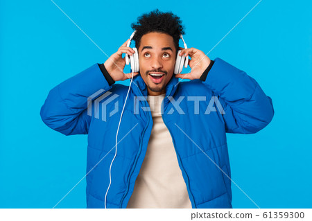 Guy enjoying nice soft sound of new headphones parents bought for christmas. Cheerful stylish hipster african american man in padded winter jacket, put on earphones listen music smiling 61359300