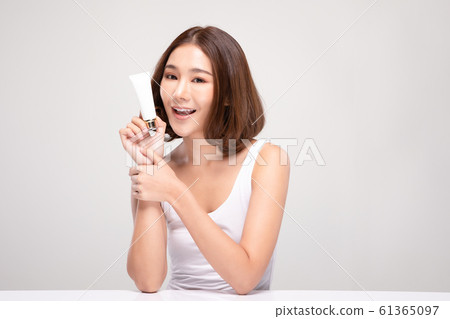 Beautiful Young Asian Woman with short hair Holding luxury white clean tube smile feeling so happy and cheerful with healthy Clean and Fresh skin,isolated on gray background,Beauty Cosmetics Concept 61365097