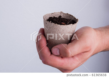 Hand holds small gardening pot with soil. Hand holds small gardening pot with soil. 61365638
