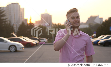 Handsome cheerful businessman talking mobile phone walking in the Street at Sunset. Handsome cheerful businessman talking mobile phone walking in the Street at Sunset. 61366956