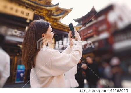 brunette girl taking photos on her phone of a pagoda in Yuyuan 61368005
