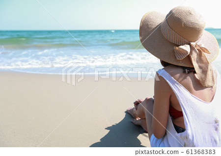 Back view portrait of sexy asian young girl in bikini and hat, looking away to tropical beach while sitting on sandy beach in nature with blue sky. Back view portrait of sexy asian young girl in bikini and hat, looking away to tropical beach while sitting on sandy beach in nature with blue sky. 61368383