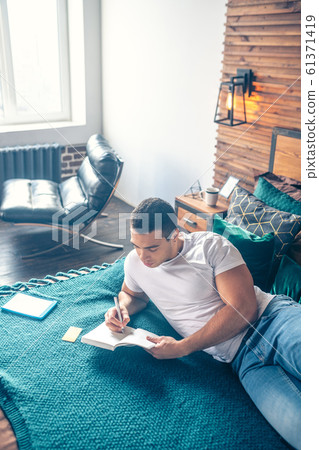 Guy writing with a pen in notebook lying on the bed. Guy writing with a pen in notebook lying on the bed. 61371419