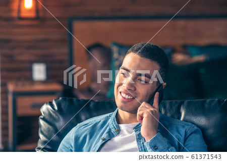 Handsome guy talking on a smartphone while at home. Handsome guy talking on a smartphone while at home. 61371543