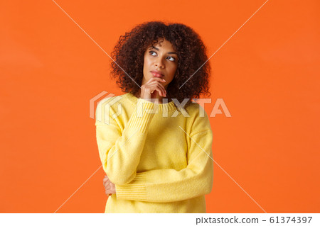 Waist-up portrait unsure, thoughtful young creative african-american female entrepreneur making new ideas, standing orange background, searching inspiration, thinking looking up 61374397