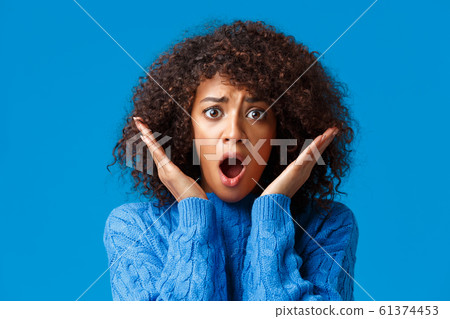 Close-up panicking, troubled and shocked african-american woman with curly afro haircut, gasping concerned, raise hands near face, staring at terrible bad scene, standing scared blue background 61374453