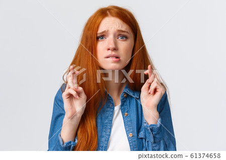 Close-up portrait nervous cute and hopeful caucasian redhead woman begging god for dream come true, cross fingers good luck, bite lip worried, praying over white background 61374658